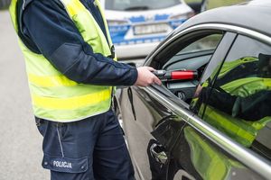 na zdjęciu policjant przy samochodzie z alkomatem w ręce