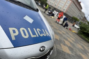 na zdjęciu fragment radiowozu, a za nim uczestnicy zawodów w trakcie zmagań