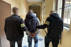 na zdjęciu kryminalni prowadzą zatrzymanego korytarzem komendy