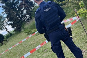 na zdjęciu policjant przy wygrodzonym terenie taśmą, gdzie leży pocisk