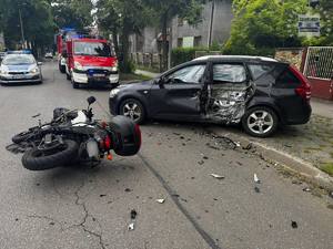 na zdjęciu motocykl i pojazd z uszkodzeniami na drodze, obok radiowóz policyjny i wozy strażackie oraz inne pojazdy