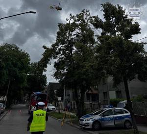 na zdjęciu policjant, radiowóz, wóz strażacki i inne pojazdy na drodze, nad nimi śmigłowiec lotniczego pogotowia ratunkowego