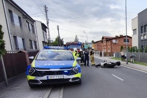 na zdjęciu radiowóz i leżący obok na jezdni motocykl, obok inne osoby