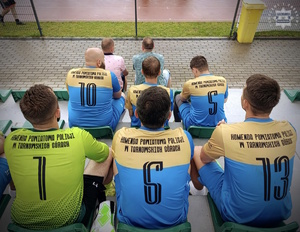 na zdjęciu policjanci w koszulkach sportowych siedząc tyłem do obiektywu na trybunie