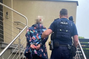 na zdjęciu policjant prowadzi poszukiwaną kobietę schodami do budynku komendy