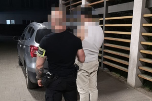 na zdjęciu policjant po cywilu z opaską na ramieniu, trzyma za trzymanego za rękę