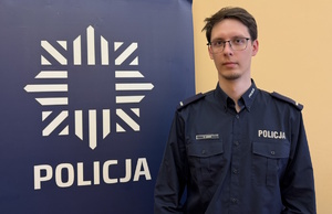 na zdjęciu dzielnicowy Janus przy banerze z napisem policja