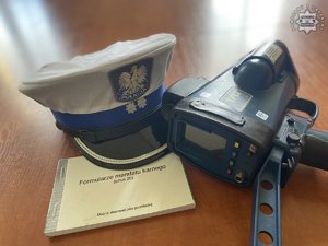na zdjęciu policyjna czapka, miernik prędkości i bloczek mandatowy