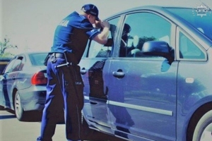 na zdjęciu policjant zaglądający do wnętrza samochodu osobowego