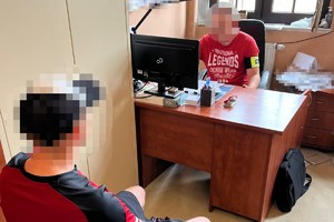na zdjęciu policjant za biurkiem, a przed nim zatrzymany na krześle