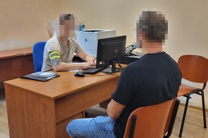 na zdjęciu policjant po cywilu przy biurku, a przed nim zatrzymany