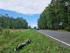Na zdjęciu motorower w rowie obok na jezdni w oddali policyjny radiowóz