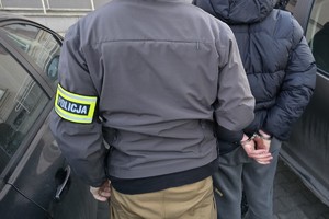 na zdjęciu policjant po cywilu z opaską na ramieniu z zatrzymanym przy samochodzie