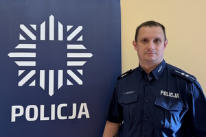 policjant w niebieskim mundurze, obok niebieski baner z napisem policja