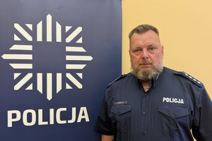 na zdjęciu dzielnicowy Konieczny przy banerze z napisem policja