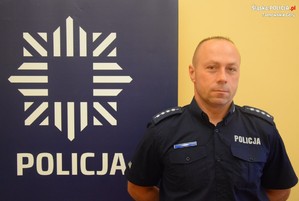 na zdjęciu dzielnicowy Kędzia przy banerze z napisem policja