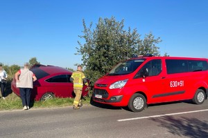 na zdjęciu samochód w rowie, obok wóz strażacki, osoby i strażak przy nich