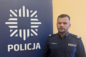 dzielnicowy Kracik przy banerze z napisem policja