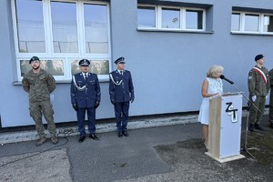 na zdjęciu policjanci i wojskowy na placu szkolnym, obok przy mównicy pani dyrektor w trakcie przemówienia