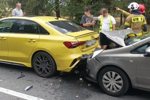 na zdjęciu dwa samochody na jezdni z uszkodzeniami, obok nich osoby i strażacy