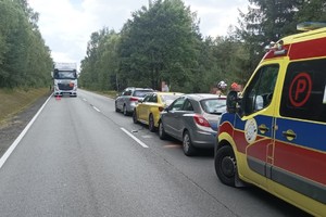 na zdjęciu trzy samochody na jezdni z uszkodzeniami, obok nich osoby i strażacy, za nimi karetka pogotowia, przed nimi ciężarówka