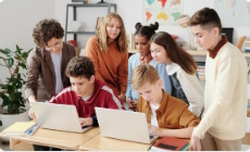na zdjęciu osoby przy biurku gdzie leża dwa laptopy