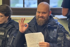 na zdjęciu policjant z kartkami w ręce uśmiechający się do zdjęcia