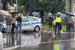 na zdjęciu radiowóz i policjant na skrzyżowaniu, obok ludzie