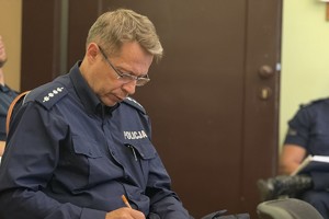 na zdjęciu siedzący policjant w trakcie sporządzania zapisków w notatniku