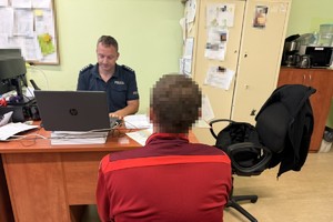 na zdjęciu policjant za biurkiem, przed nim mężczyzna w czerwonej bluzie