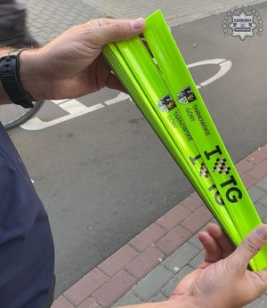 na zdjęciu dłonie policjanta trzymające opaski odblaskowe