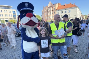 na zdjęciu policyjna maskotka sznupek na płycie tarnogórskiego rynku w trakcie zlotu pojazdów zabytkowych w towarzystwie różnych osób robiący zdjęcia