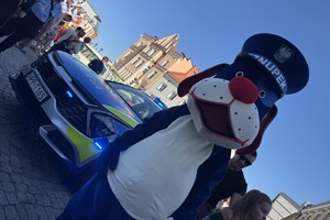 na zdjęciu policyjna maskotka sznupek na płycie tarnogórskiego rynku w trakcie zlotu pojazdów zabytkowych w towarzystwie różnych osób robiący zdjęcia