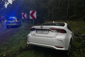 na zdjęciu biały samochód w rowie, obok na jezdni radiowóz i w oddali wóz strażacki