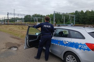 na zdjęciu policjant przy radiowozie niedaleko torowiska kolejowego