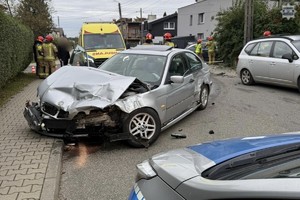 Na zdjęciu fragment radiowozu przednim rozbity pojazd za nim karetka i strażacy