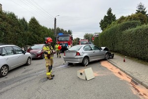 Na zdjęciu Strażak obok rozbitego samochodu na jezdni w oddali wozy strażackie i inny Strażak
