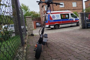 na zdjęciu elektryczna hulajnoga, a za nią na jezdni karetka pogotowia