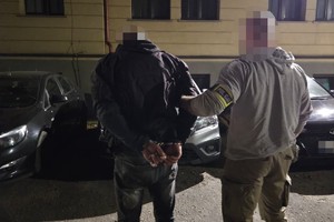 na zdjęciu policjant po cywilu z zatrzymanym na parkingu przy pojazdach