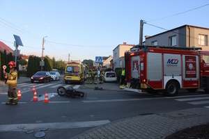 na zdjęciu skrzyżowanie i leżący na nim motorower, obok strażacy i ich wóz oraz karetka