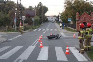 na zdjęciu skrzyżowanie i leżący na nim motorower, obok strażacy i ich wóz oraz karetka