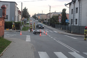 na zdjęciu skrzyżowanie i leżący na nim motorower, obok strażacy i ich wóz oraz karetka