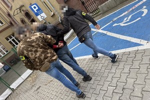 na zdjęciu kryminalni prowadzą zatrzymanego do budynku