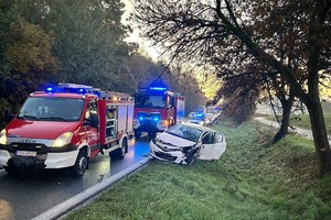 na zdjęciu wozy strażackie i radiowóz przy uszkodzonym samochodzie w rowie
