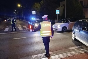 na zdjęciu policjant na jezdni po zmroku, obok samochody