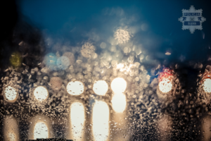 na zdjęciu krople wody na szybie, a za nią widoczne światła