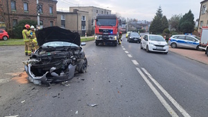 na zdjęciu uszkodzony samochód na jezdni, obok strażacy i inne osoby oraz pojazdy