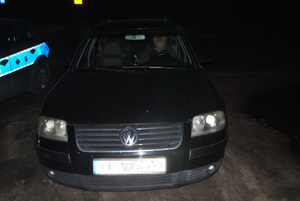 na zdjęciu czarny samochód po zmroku zaparkowany obok radiowozu