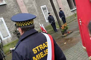 na zdjęciu funkcjonariusze straży miejskiej a przed nimi przemawiająca do mikrofonu osoba