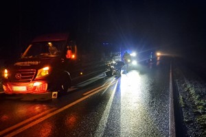 na drodze po zmroku osobowy bus, przy nim osoby i policjanci z radiowozem kierujący ruchem